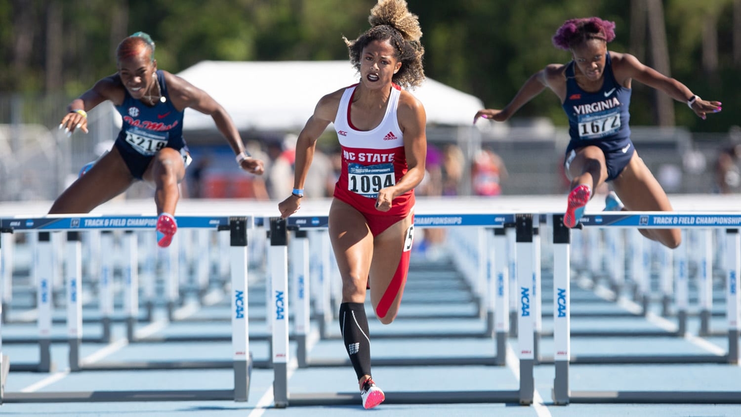 Gabrielle Cunningham jumps over a hurdle at a track and field event.