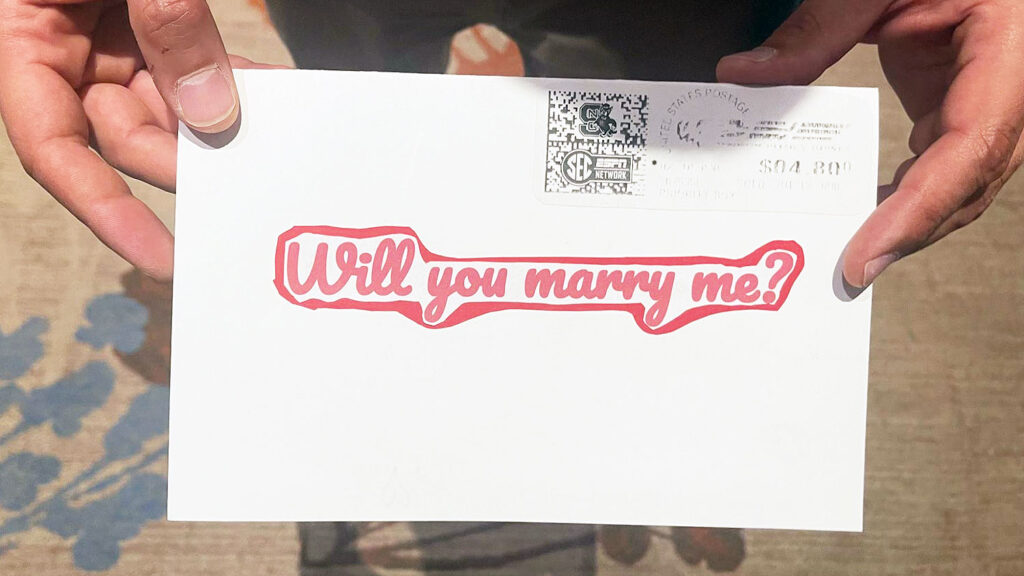 hands holding envelope that says "Will you marry me?"