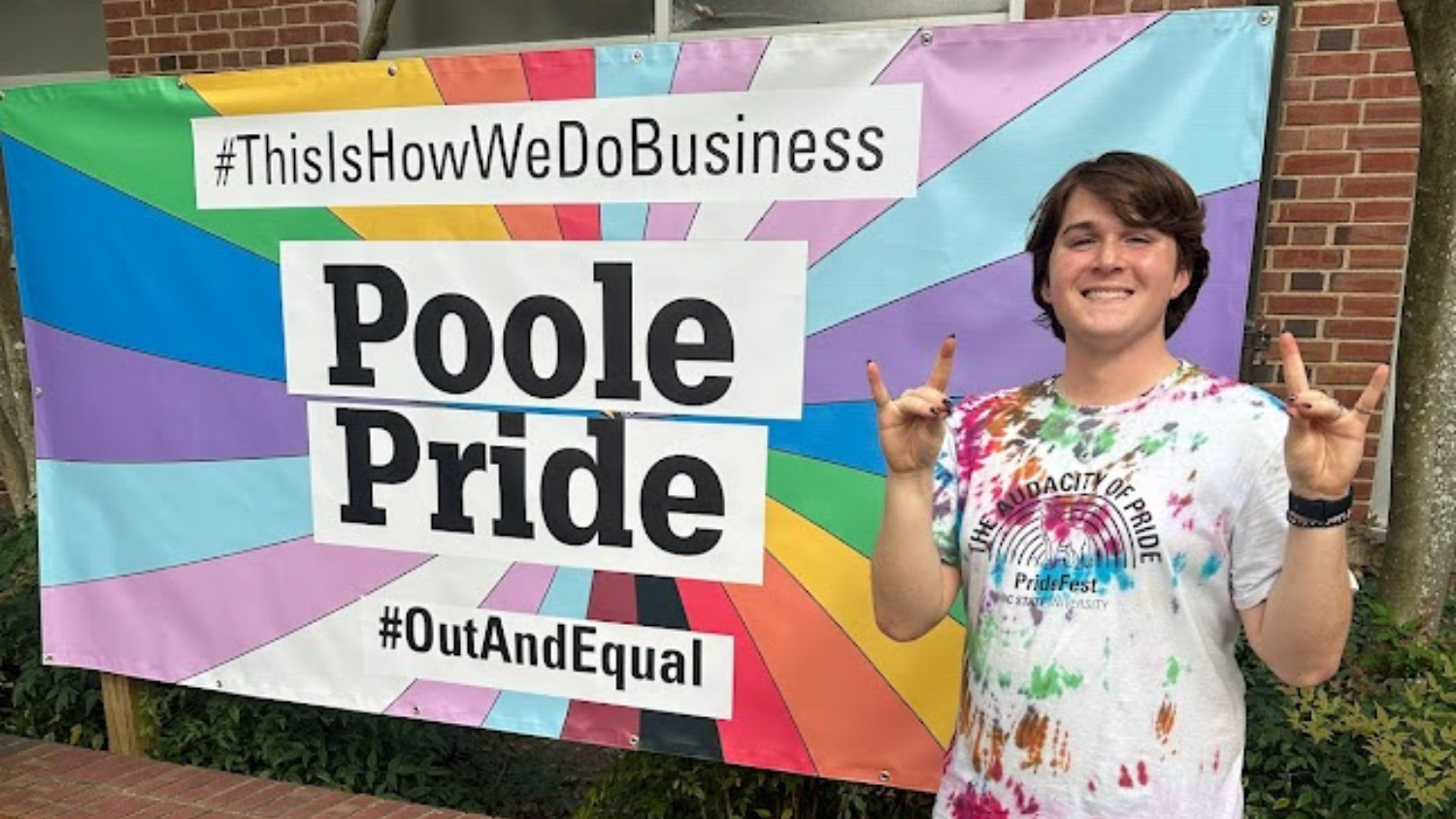 Queer Business Student Association Founder Colin Adams next to Poole pride banner.