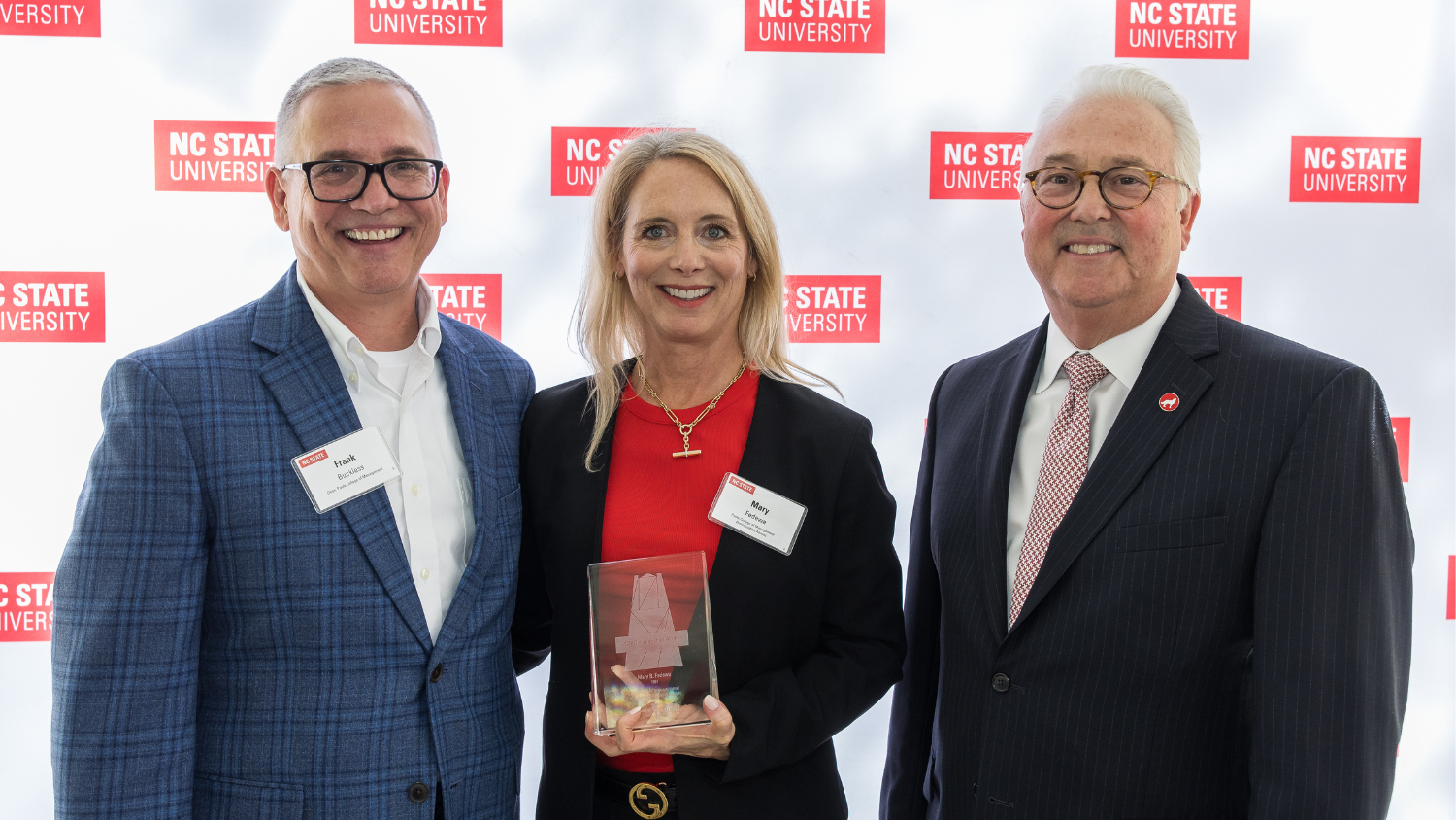 Mary Fedewa holding Poole College’s 2024 Distinguished Alumni Award next to Dean Frank Buckless and Chancellor Randy Woodson