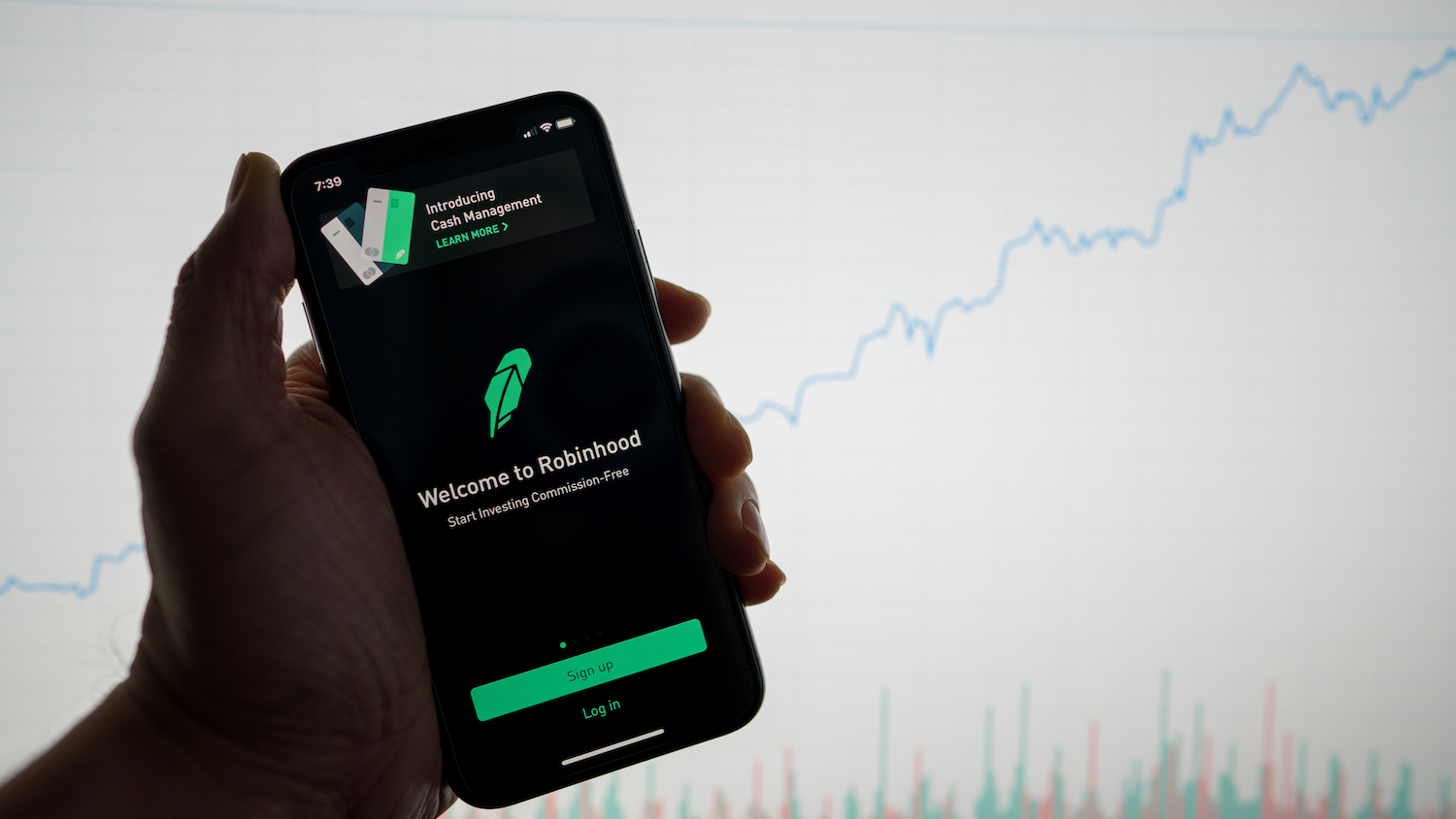 Robinhood app on phone with white financial stock chart with price rising upward positive in background