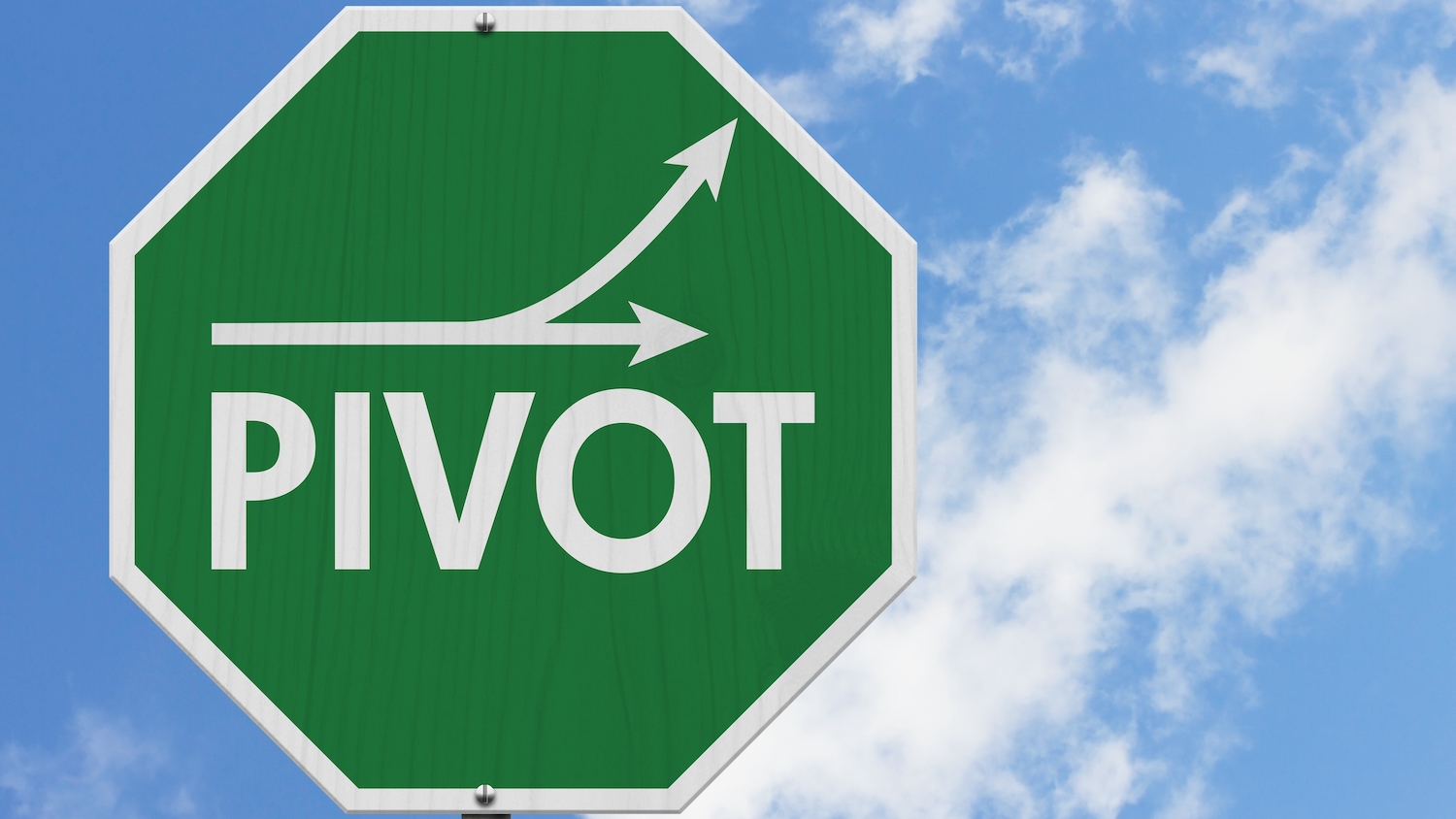 A green street sign with the word "PIVOT" against a background of blue sky and white clouds
