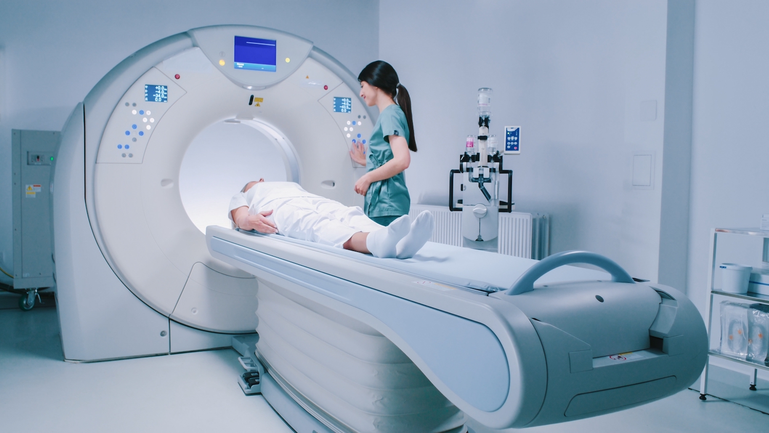 A medical professional talks to a patient, lying prone, as the patient enters an MRI scanner