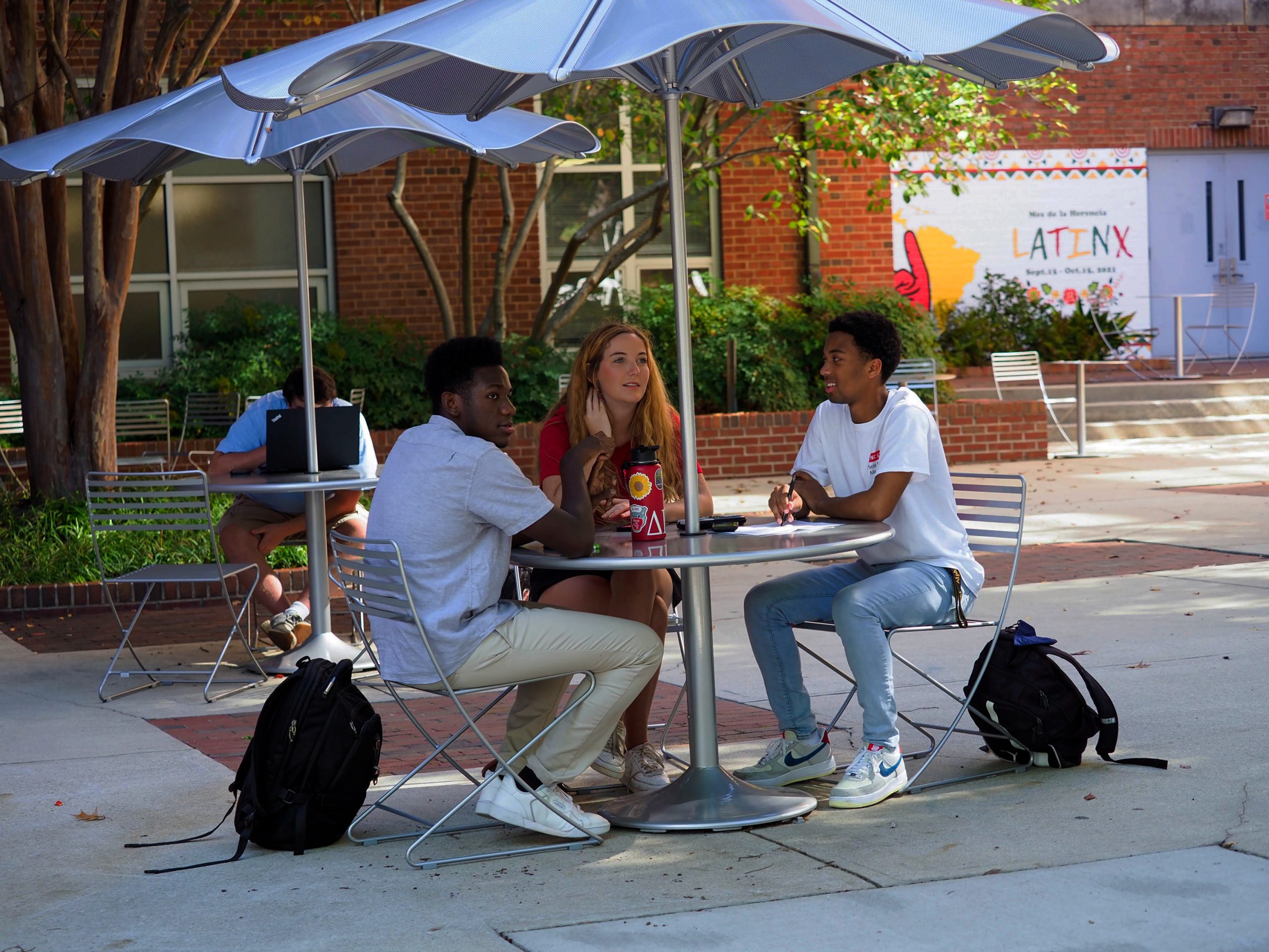 Three students sit at a table outdoors in the Nelson Hall courtyard